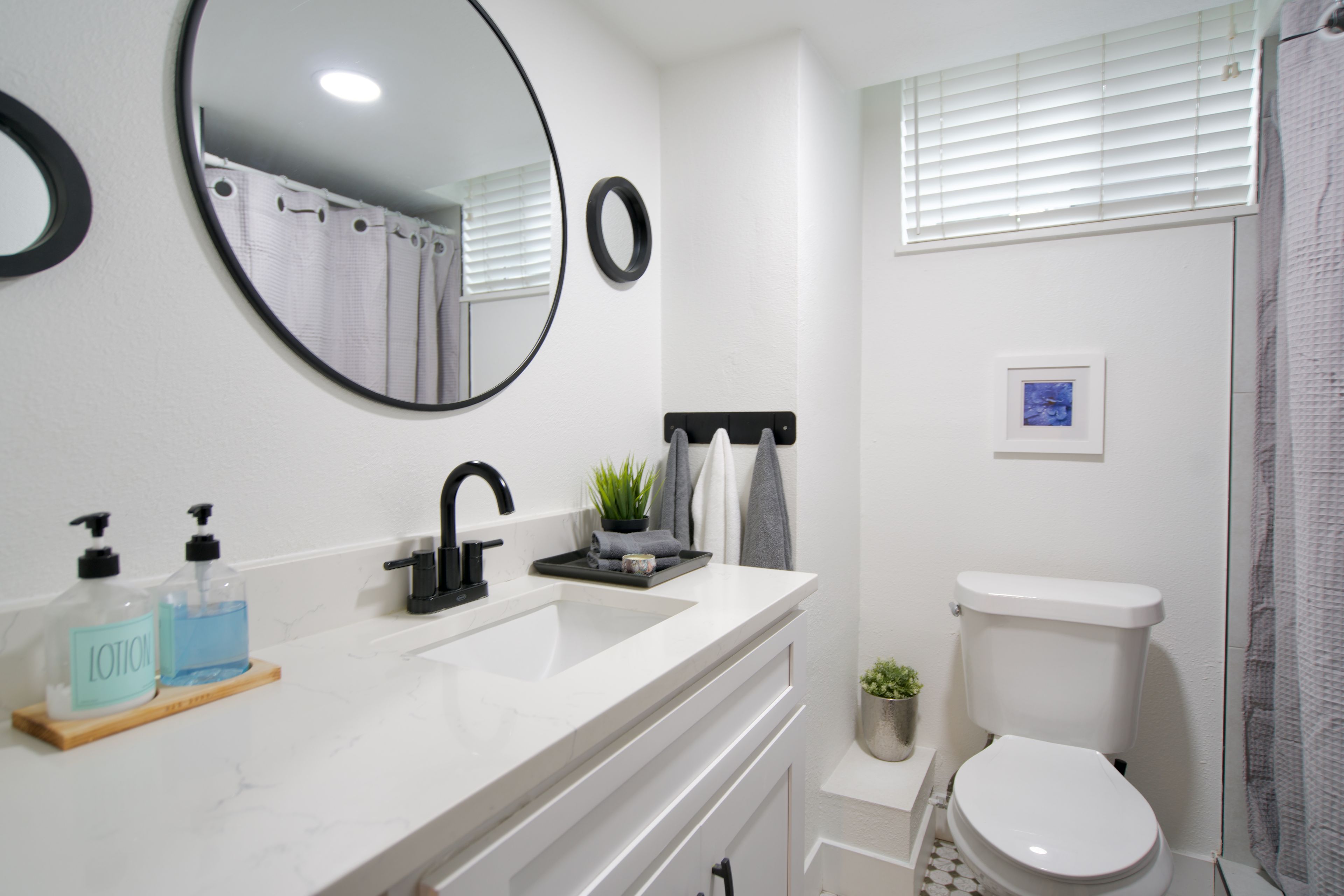 A bathroom with a white sink, black faucet, and a toilet. There are two bottles of lotion on the counter.