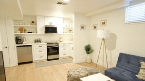 Una cocina moderna con armarios blancos, un microondas y un lavavajillas. Hay un comedor con una mesa blanca y un sofá azul.