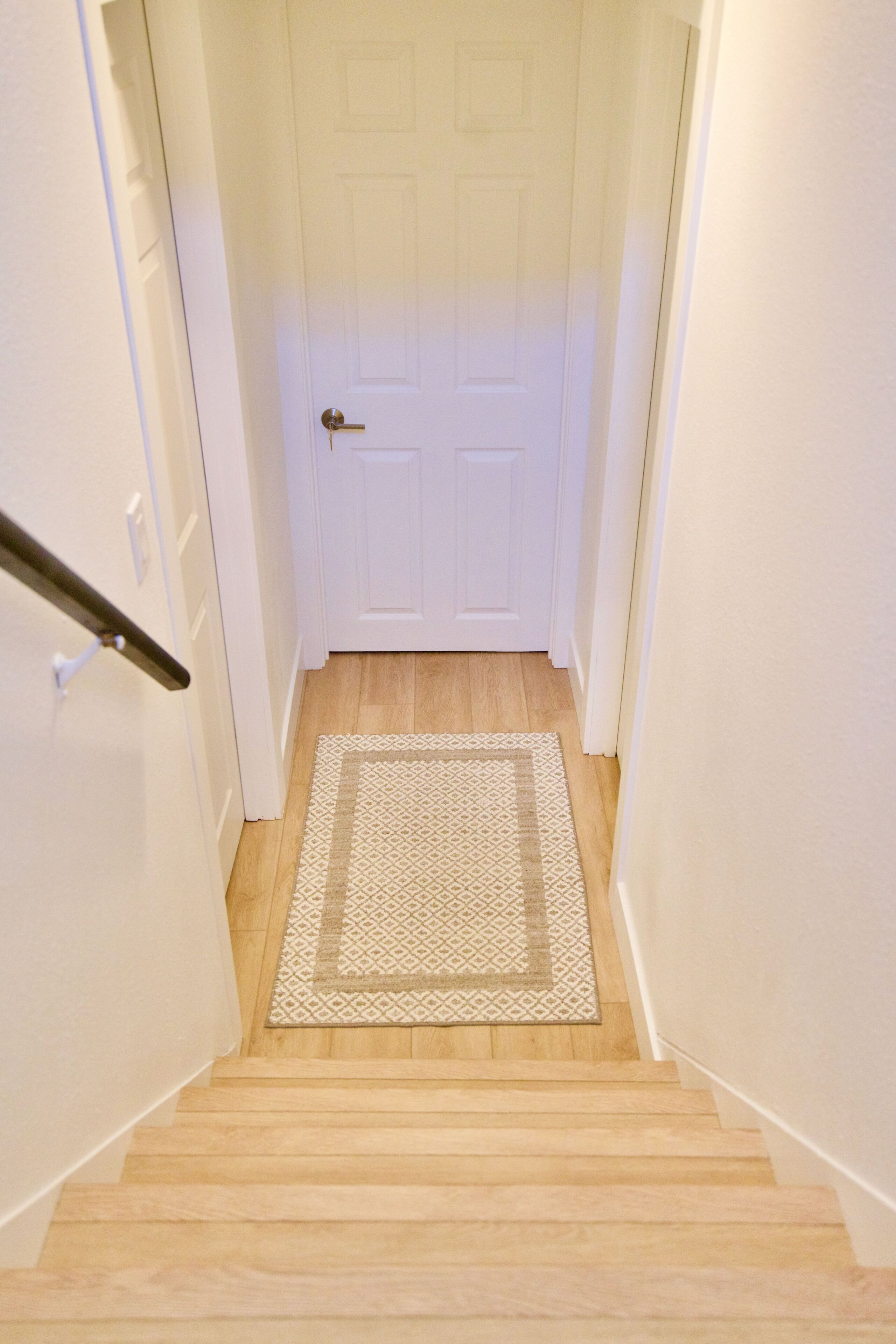 Una escalera con piso de madera que lleva a una puerta blanca con picaporte.
