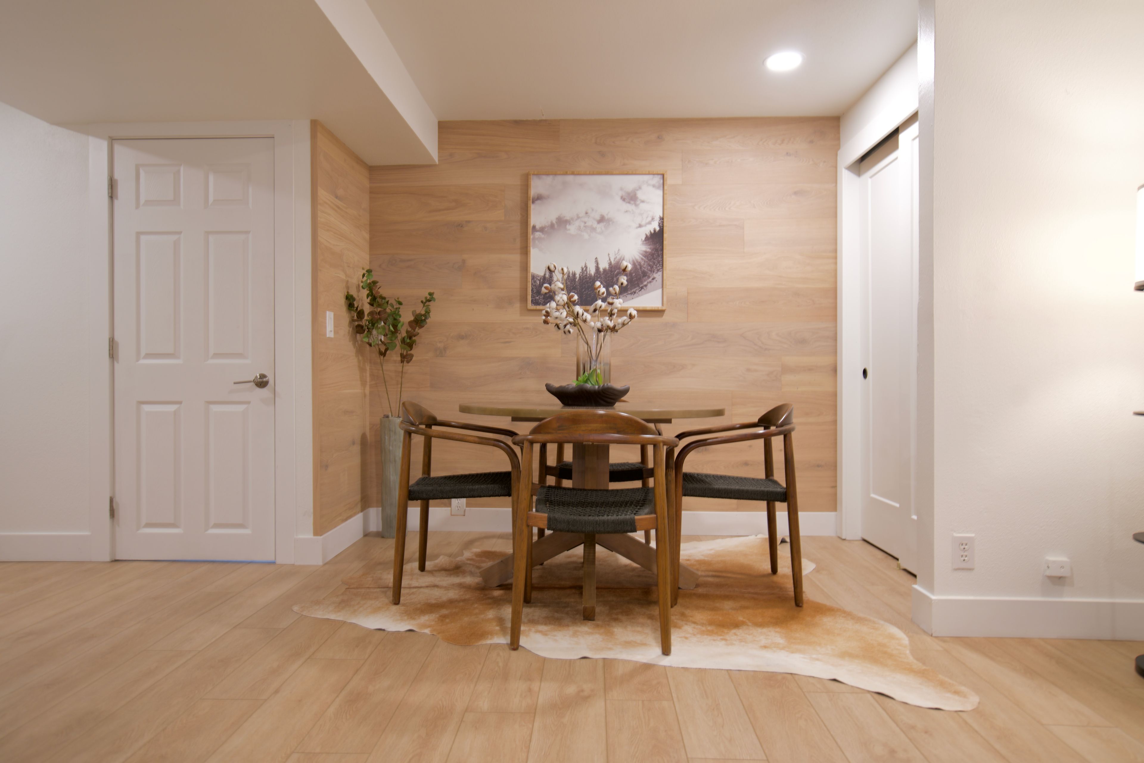 Un coin repas avec une table en bois, quatre chaises, un vase de fleurs et un tableau accroché au mur.