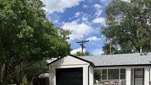 Een gelijkvloers huis met garage, een voortuin met stoelen en een verzorgde tuin met een grindpad.