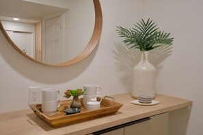 Un plan de travail de cuisine sur lequel se trouve un plateau en bois contenant des tasses blanches, un petit vase avec une plante et un pichet blanc.