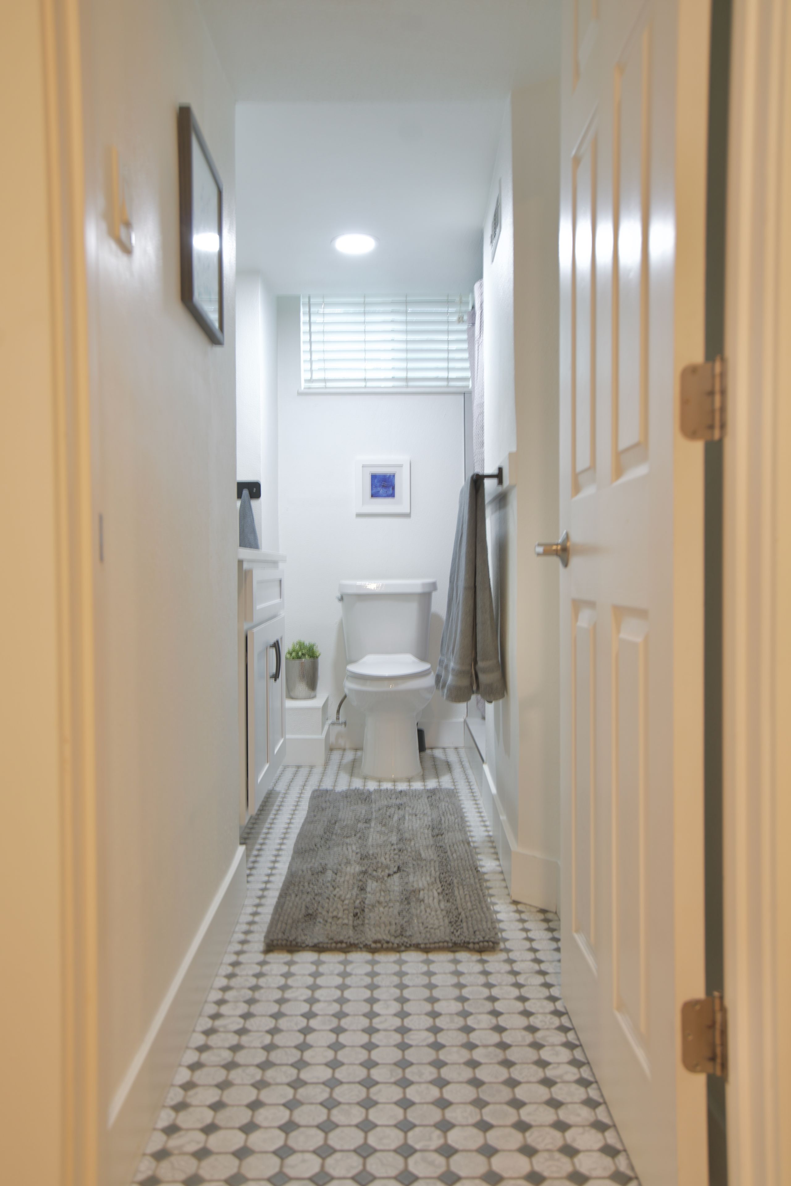 Un pasillo estrecho que conduce a un baño con inodoro, lavabo y ventana con persianas.