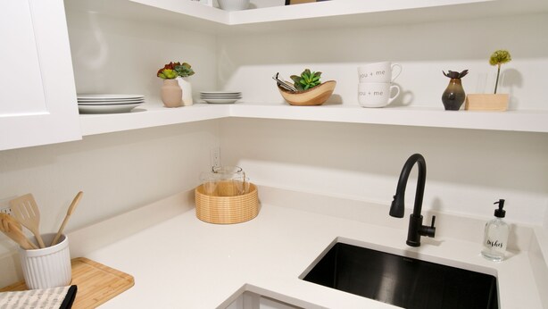 Una cocina moderna con armarios blancos, un lavamanos negro y una tabla de cortar de madera.