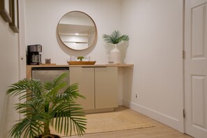 Une cuisine de taille réduite, équipée d’une machine à café, agrémentée d’une plante et ornée d’un miroir au mur.