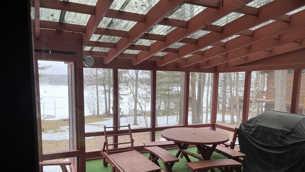 Un espace extérieur aménagé, abrité et doté de tables et de bancs en bois, d’un sol recouvert d’un gazon synthétique vert et offrant une vue sur un paysage enneigé grâce à de grandes fenêtres.