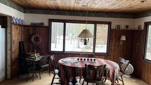 Un espace repas doté d’un plafond en bois, de grandes fenêtres et d’une table ronde entourée de chaises.