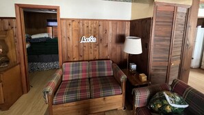 Une pièce chaleureuse avec un canapé à carreaux, une petite table avec une lampe et une tête de lit en bois sur laquelle est inscrit le mot « Lake ».