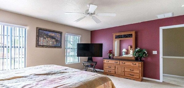 Un dormitorio con cama, televisor, cómoda y ventilador de techo.