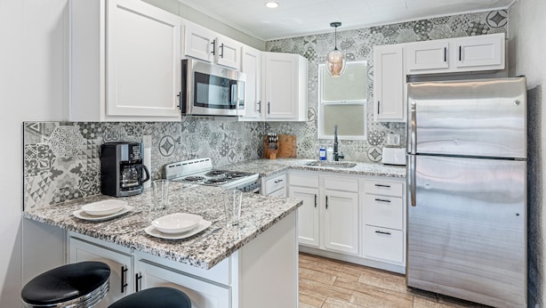 Una cocina moderna con armarios blancos, un refrigerador de acero inoxidable, un microondas, una cafetera y un salpicadero decorativo.