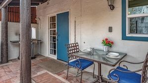 Un patio con mesa y sillas, una puerta azul y un aplique de pared.