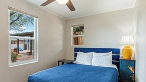Un dormitorio con cama, mesita de noche, lámpara y ventana.