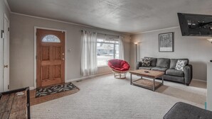 A living room with a wooden door, a red chair, a grey sofa, and a mounted TV.