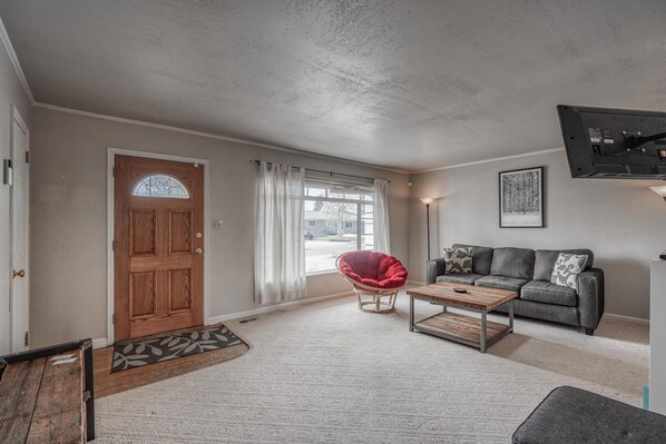 A living room with a wooden door, a red chair, a grey sofa, and a mounted TV.