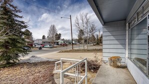 A residential street with a house featuring a concrete staircase and a large tree in the foreground.