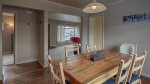 A dining area with a wooden table and chairs, a chandelier, and a view of a red chair through an open door.