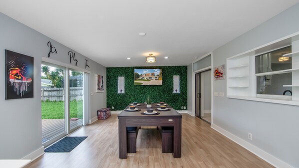 A modern dining area with a table set for four, a green wall with a TV, and a sliding glass door leading to a backyard.