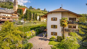 Ein zweistöckiges Gebäude mit Balkon, umgeben von üppigem Grün und einem Weinberg.