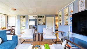 Una sala de estar moderna con una pared azul de acento, un televisor de pantalla plana y un comedor con una mesa y sillas de madera.