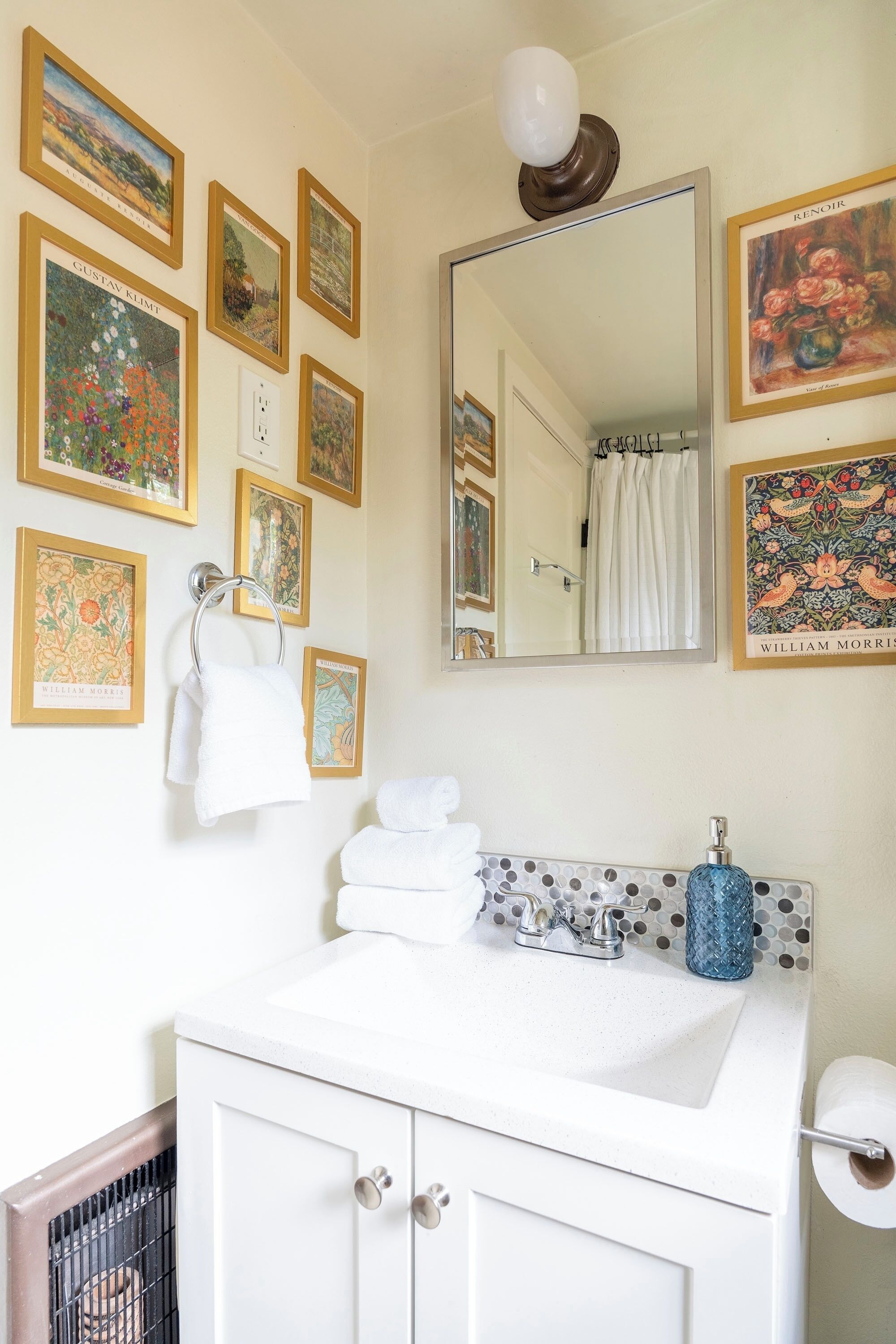 Un baño con un lavamanos blanco, un espejo y obras de arte enmarcadas en la pared.