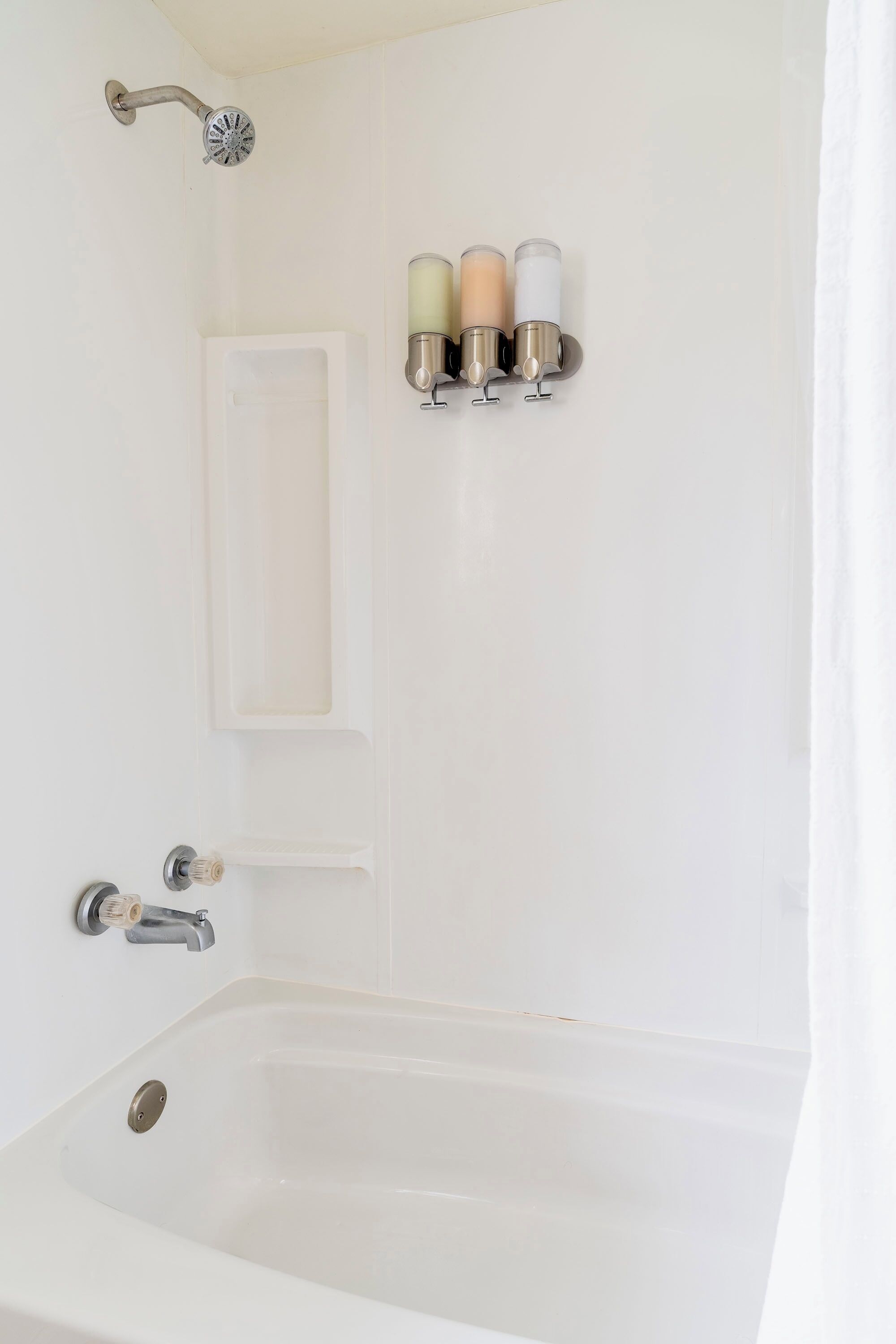 A bathroom with a bathtub, a showerhead, a towel rack with three candles, and a door.