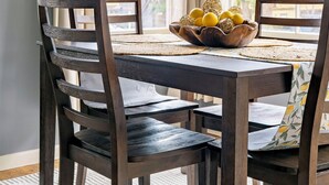 Una mesa de comedor con un cuenco tejido de limones y naranjas, rodeada de sillas de madera oscura y un mantel tejido.