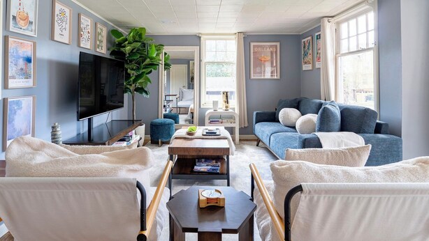 Una sala de estar con un televisor de pantalla plana grande, un sofá azul, un sillón blanco y una mesa de centro.