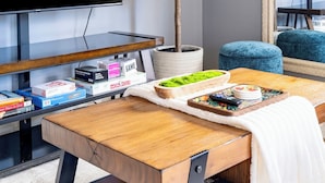 Una sala de estar moderna con un televisor de pantalla plana grande, una mesa de centro de madera, una planta en maceta y un espejo.