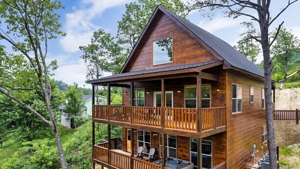 Eine zweistöckige Holzhütte mit Balkon, großen Fenstern und einem Whirlpool.