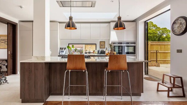 A modern kitchen with a central island, two bar stools, pendant lighting, and a view of the outdoors. - Highgate - Luxury 4-Bedroom Spacious House with Indoor Pool (London)
