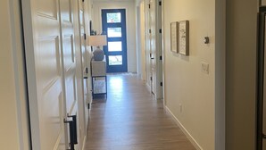 A hallway with wooden flooring, white walls, and a door at the end leading to a bright room. - Clean, Comfortable, and Modern CDA Retreat inside Gated Community. (Coeur d'Alene)