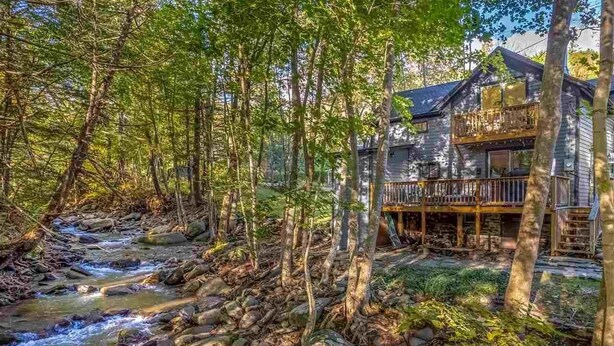 A rustic cabin with a wooden deck and a stream running through the forest. - Stream Come True! Ski, hike, spa, flow, relax... (Chichester)
