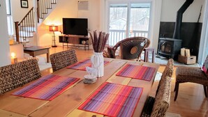 A dining area with a wooden table, woven chairs, and a television in the background. - Stream Come True! Ski, hike, spa, flow, relax... (Chichester)