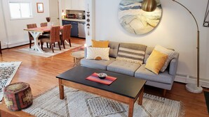A living room with a sofa, coffee table, and a dining area with chairs and a table. - Stream Come True! Ski, hike, spa, flow, relax... (Chichester)