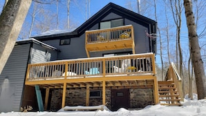 A two-story building with a balcony, surrounded by trees and covered in snow. - Stream Come True! Ski, hike, spa, flow, relax... (Chichester)