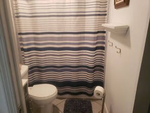 Un baño pequeño con cortina de ducha a rayas, un inodoro, un perchero y un estante pequeño.