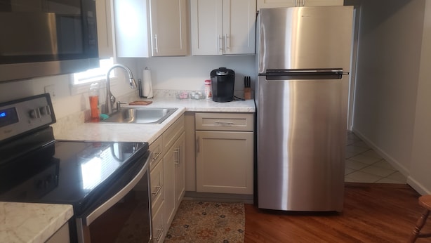 A modern kitchen with stainless steel appliances, white cabinetry, and a wooden floor.