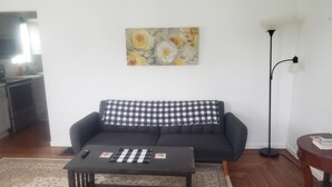 A living room with a black sofa, a checkered throw pillow, a coffee table, a floor lamp, and a painting on the wall.