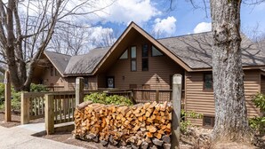 Une cabane avec un toit en pente, un revêtement extérieur en bois et une pile de bois de chauffage devant l’entrée.
