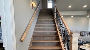 Una escalera con escalones de madera y barandal negro, que conduce a una habitación con un sofá y una mesa de centro.