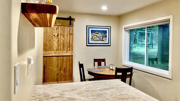Un comedor con una mesa de mármol, sillas de madera, una puerta de madera, un cuadro en la pared y una ventana con vistas a árboles.