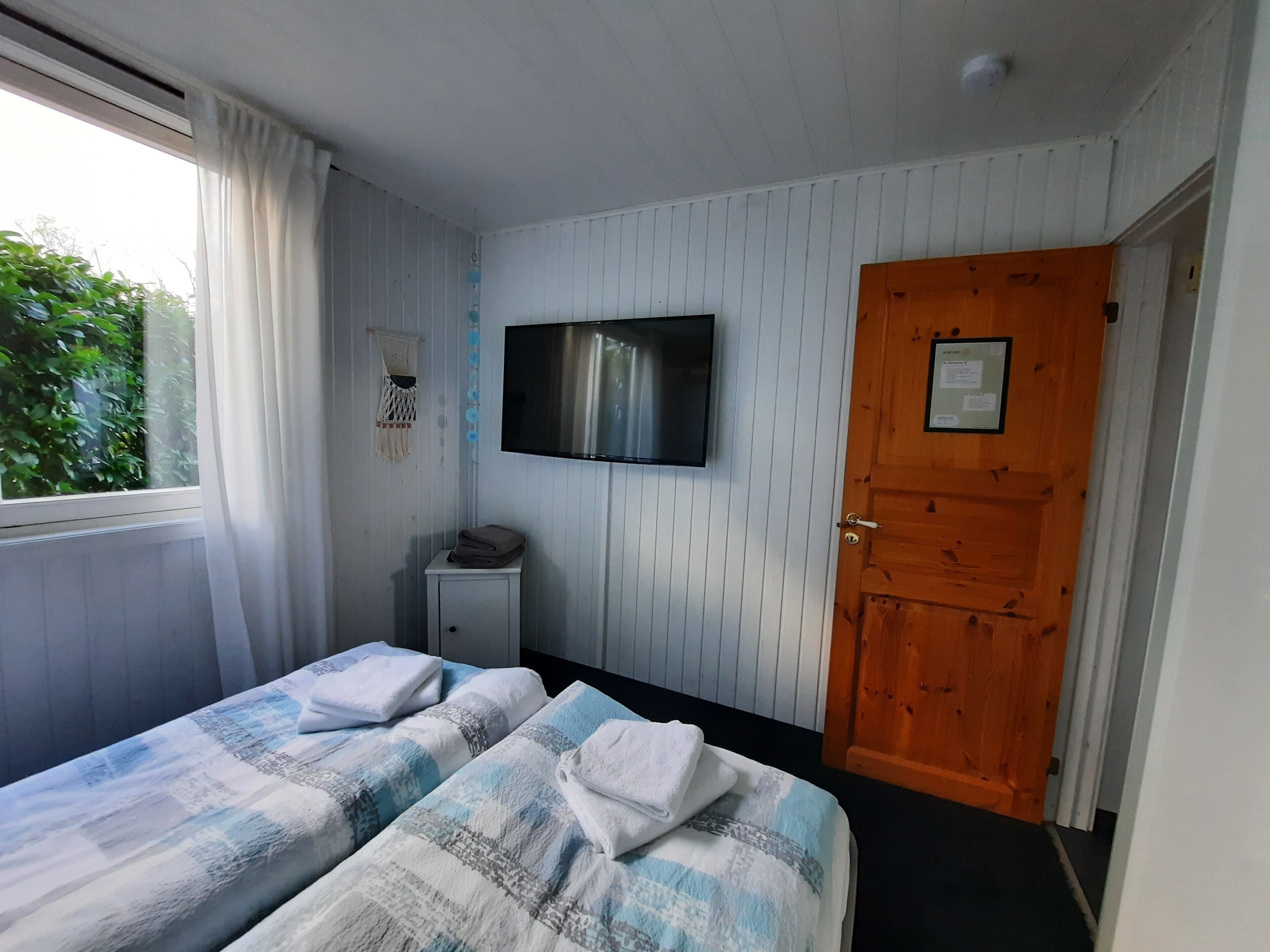 Ein Schlafzimmer mit zwei Betten, einem Fernseher, einer Holztür und einem Fenster mit Vorhängen.