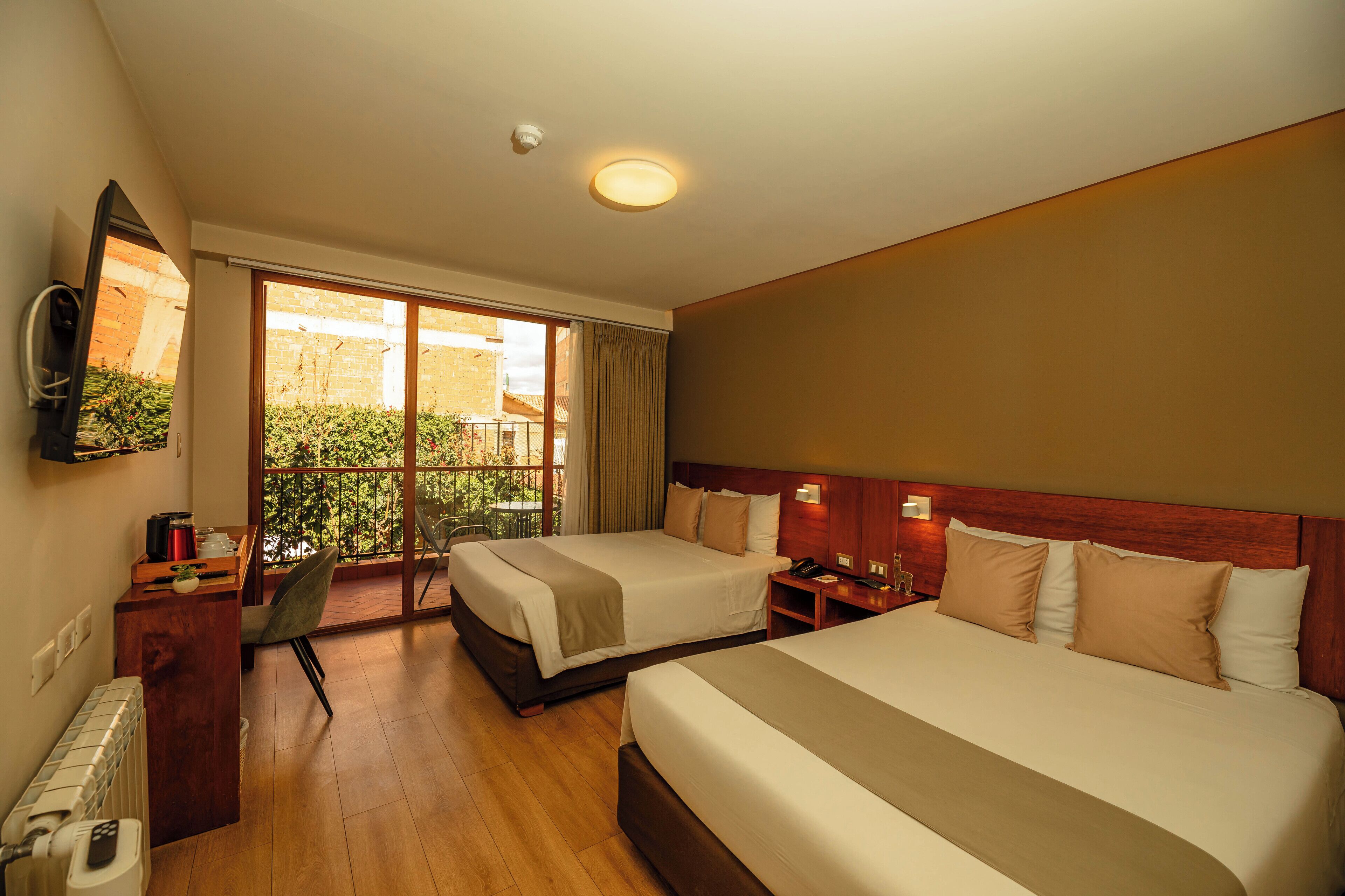 A hotel room with two beds, a desk, a chair, a TV, and a balcony with a view.
