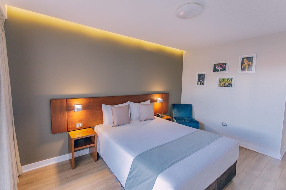 Ein modernes Hotelzimmer mit einem großen Bett, Nachttischen, einem Sessel und Wandbildern.