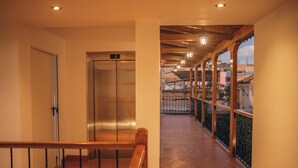 Ein Hotelgang mit Aufzug, einem Holllaufgeländer und einem Balkon mit Blick auf Gebäude.