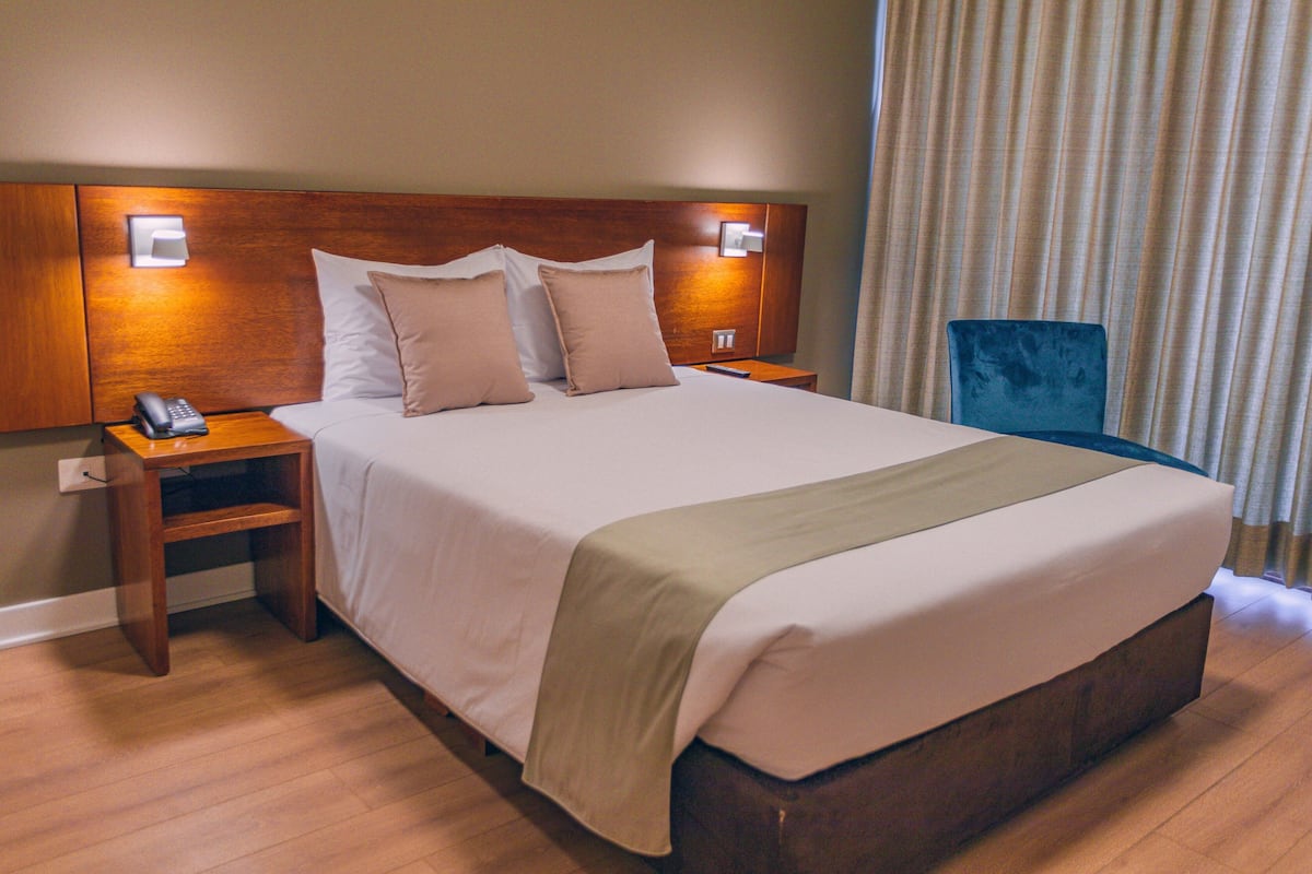 Ein Hotelzimmer mit einem großen Bett, einem Holzkopfende, Nachttischen mit Lampen und einem blauen Sessel.