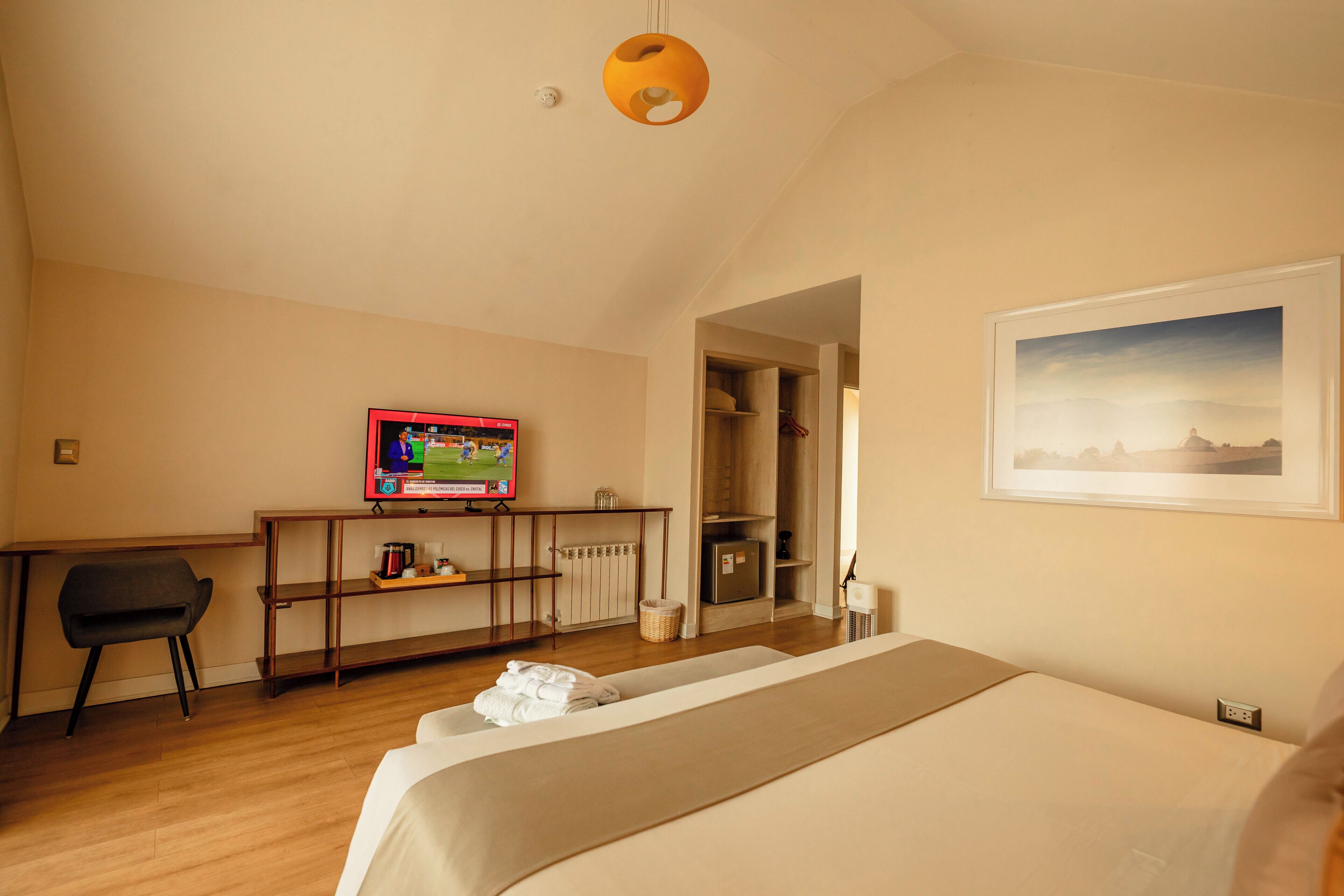 Une chambre d’hôtel avec un lit, un bureau avec une télévision, une chaise, une étagère et un tableau au mur.
