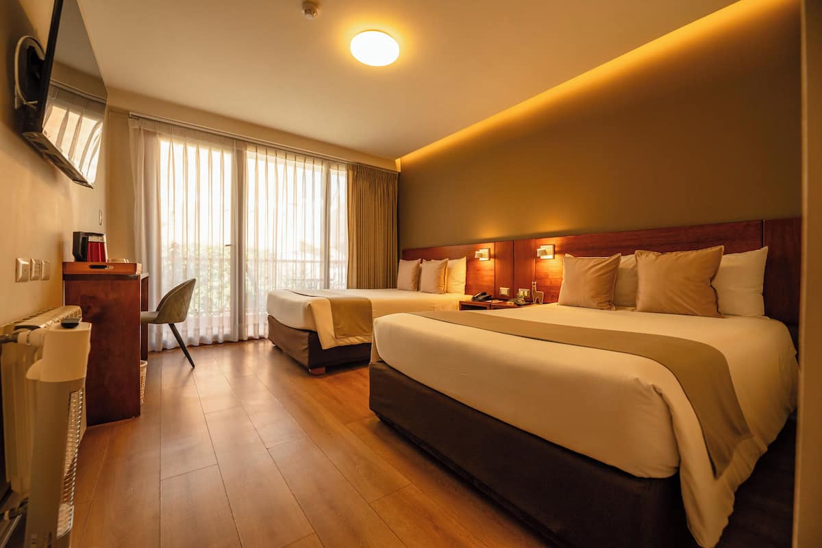 Ein Hotelzimmer mit zwei Betten, einem Schreibtisch, einem Sessel, einem Fernseher und einem großen Fenster mit Vorhängen.