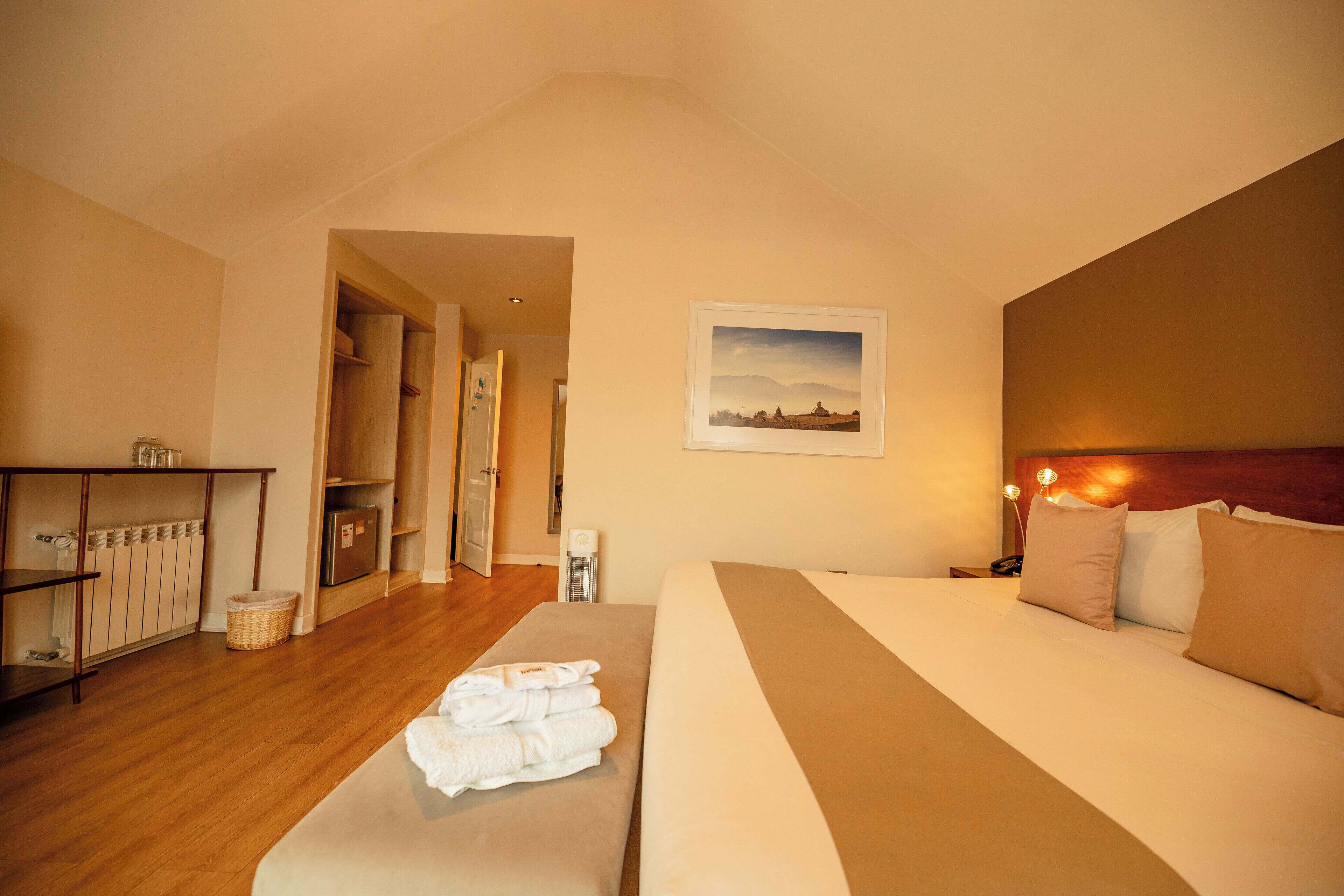 A hotel room with a bed, a bedside table, a headboard, a wall-mounted picture, and a wooden floor.