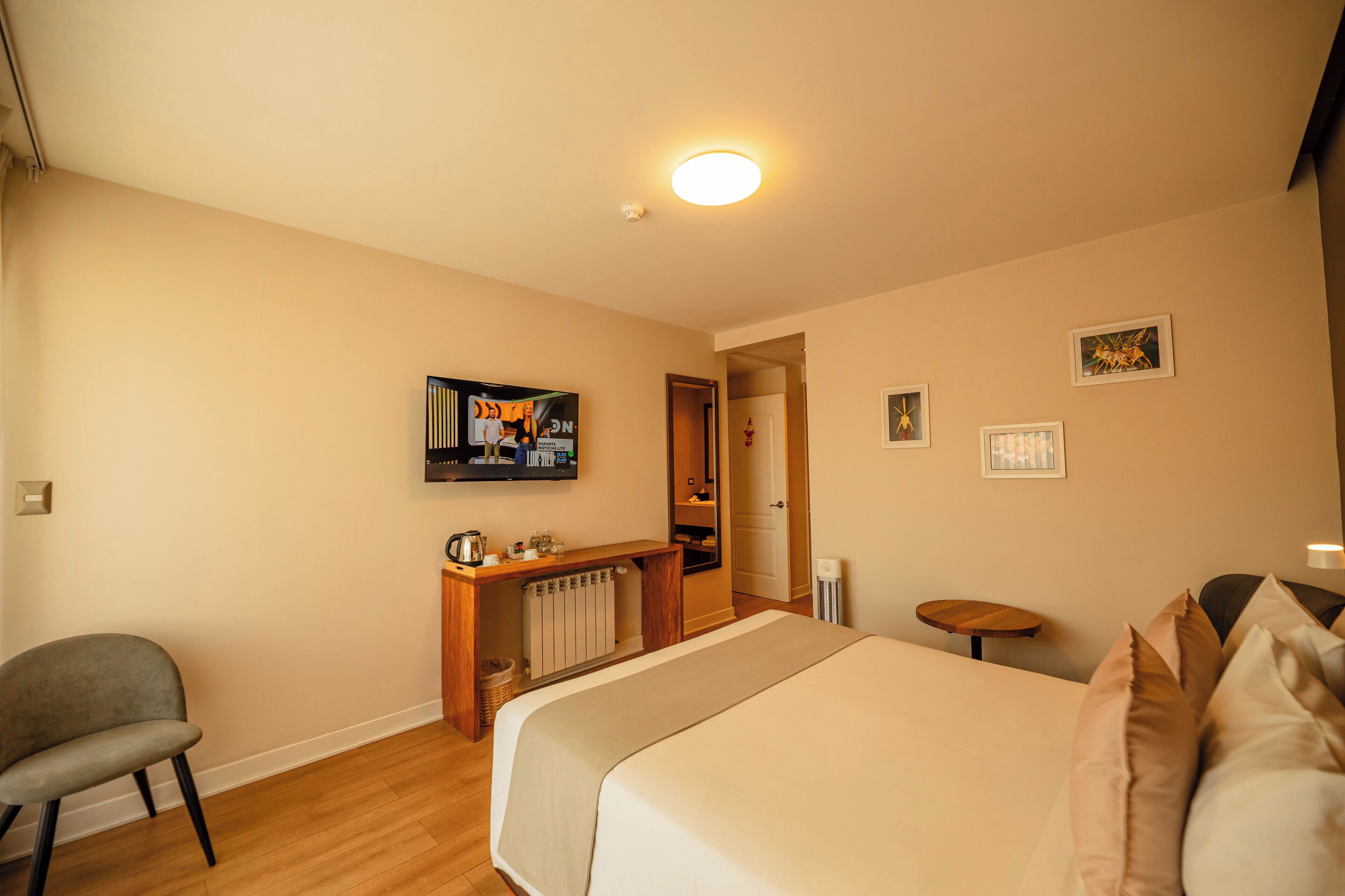 Habitación de hotel con cama, escritorio, silla, radiador, televisor y una mesita.